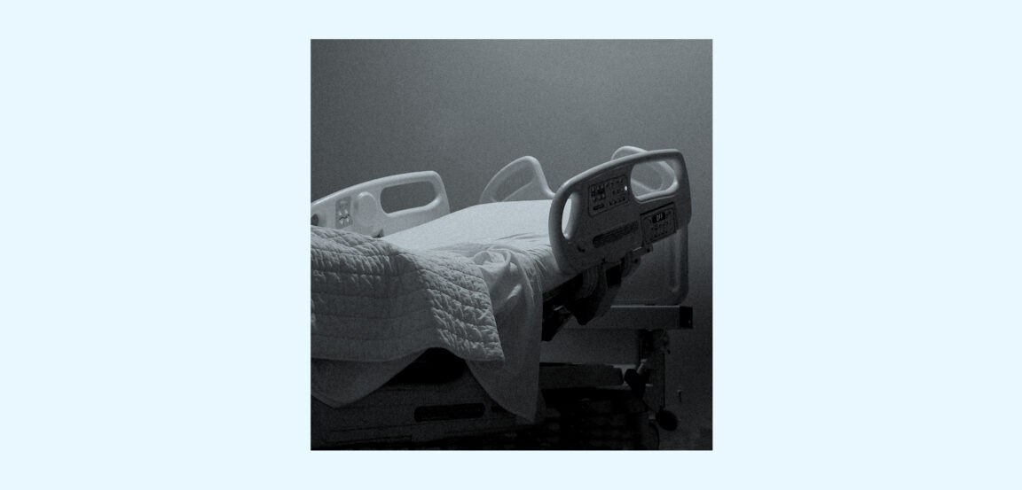 A dimly lit, empty hospital bed with raised side rails and rumpled white sheets, photographed in moody grayscale against a plain wall.