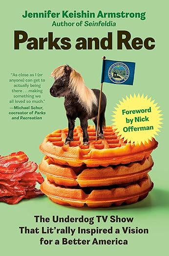 Book cover of Parks and Rec: The Underdog TV Show That Lit'rally Inspired a Vision for a Better America by Jennifer Keishin Armstrong, author of Seinfeldia. A miniature horse stands atop a tall stack of golden waffles, holding a Pawnee, Indiana flag. Strips of bacon are scattered nearby. The cover includes a foreword by Nick Offerman and a quote from Michael Schur, cocreator of Parks and Recreation.